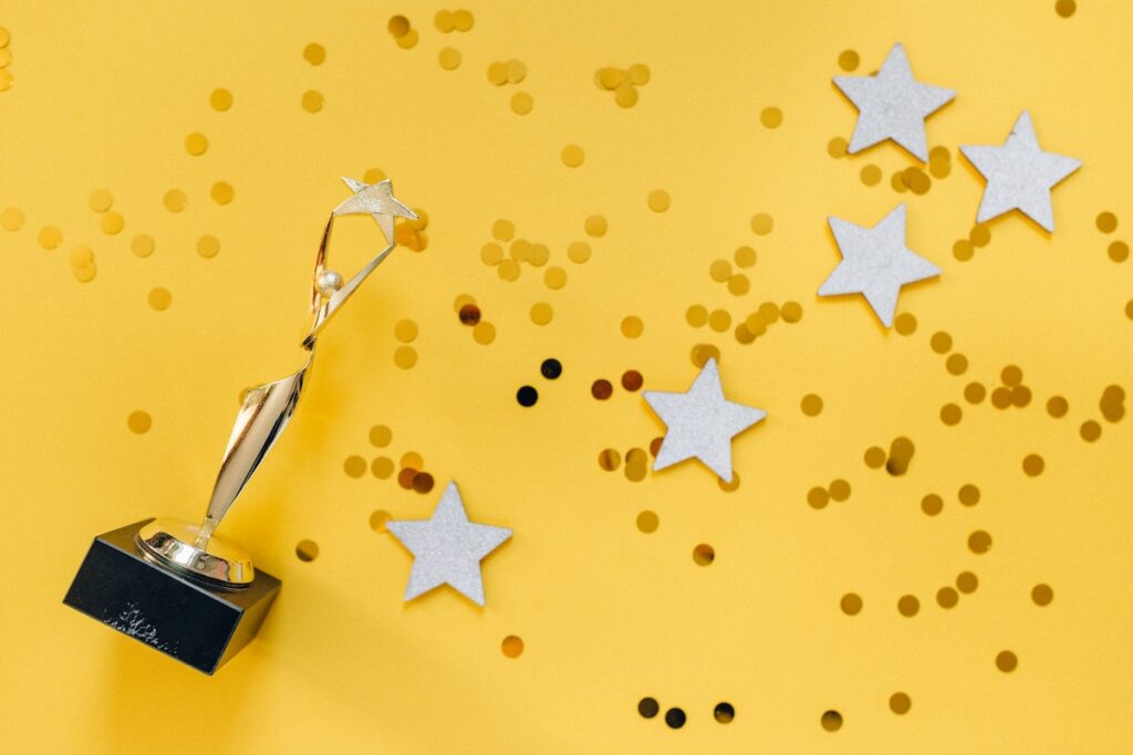 A gold trophy on a bright yellow background sprinkled with silver stars and confetti.