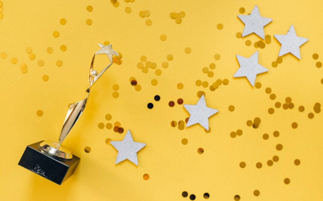 A gold trophy on a bright yellow background sprinkled with silver stars and confetti.